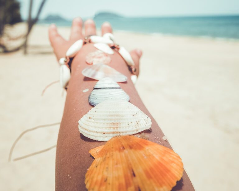 Relaxation and Leisure in summer - Seashell on tanned girl arm at tropical beach in summer. vintage color tone